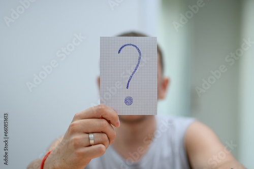 Mężczyzna trzymający na wysokości twarzy kartkę ze znakiem zapytania
