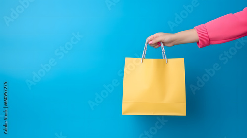 Gros plan sur une main d'une femme avec un sac de magasin pendant les soldes. En arrière plan, un fond bleu. 