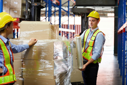 factory worker or warehouser wrapping stretch film parcel on pallet covered cardboard boxed in warehouse storage