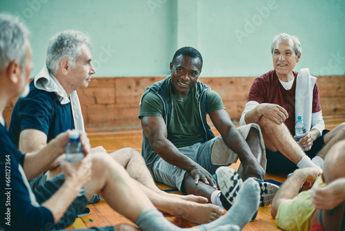 Diverse group of male senior friends sitting on the floor of a gym after playing basketball