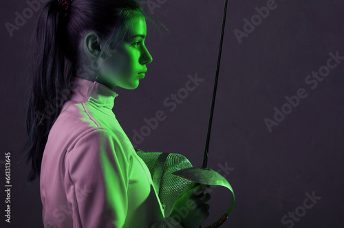 Young woman fencer profile portrait with fencing equipment holding sword in her hand