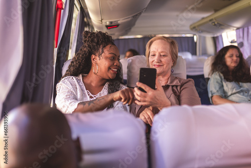 Jovem ensinando mulher idosa a usar o aplicativo de transporte urbano em seu smartphone, durante viagem de onibus.