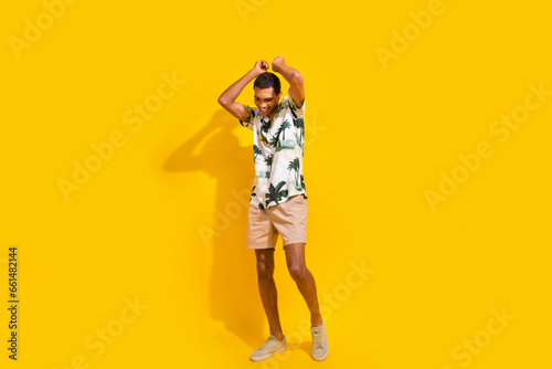 Full body photo of attractive young man dancing raise arms have fun dressed stylish palms print clothes isolated on yellow color background
