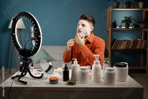 Male blogger recording tutorial video for his beauty blog about skincare routine. Vlogger applying face mask, recording video for social network. Blogging