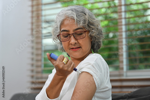 Portrait of a Diabetic mature woman taking an insulin shot on her arm. Diabetes and elderly health care concept