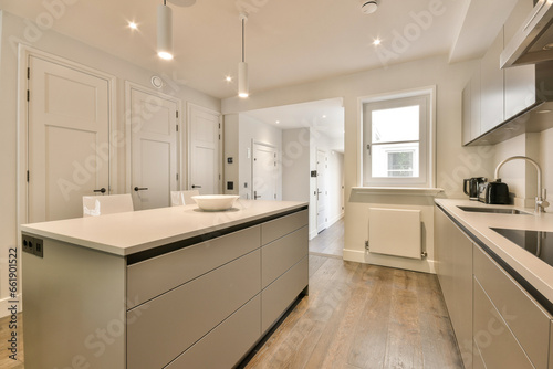 a modern kitchen with white cabinets and wood flooring in the middle of the room, looking towards the dining area