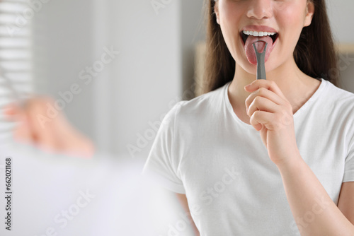 Woman brushing her tongue with cleaner indoors, closeup. Space for text