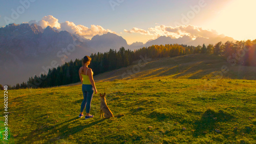 AERIAL: Attractive woman admires view of the mountains on a hilltop with her dog