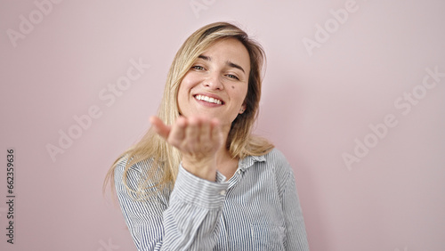 Young blonde woman smiling confident blowing kiss over isolated pink background