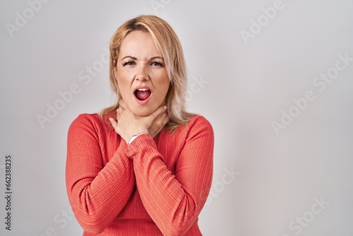 Blonde woman standing over isolated background shouting suffocate because painful strangle. health problem. asphyxiate and suicide concept.