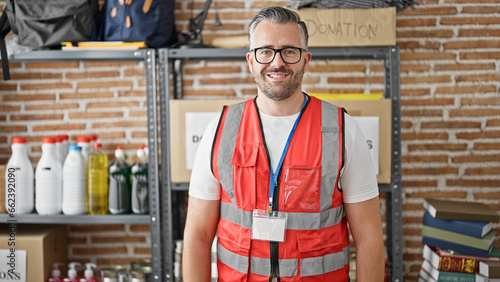 Grey-haired man volunteer smiling wearing vest at charity center