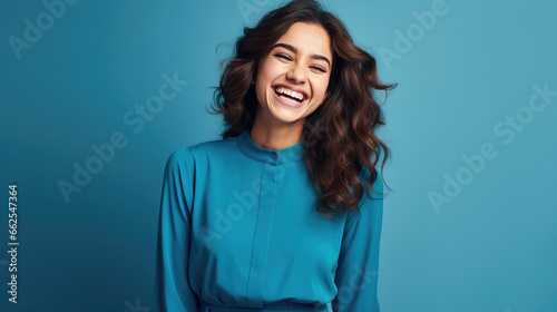 Happy ultra beautiful business girl, smiling and laughing, wearing bright blue clothe. Bright blue solid background similar to the dress color.