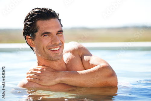 Infinity pool, portrait and happy man swimming outdoor for travel, freedom or summer holiday at resort. Relax, smile and face of male swimmer in nature for luxury getaway at villa, spa or hotel trip