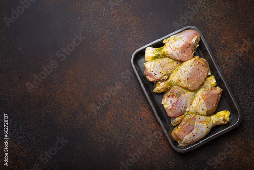 Raw uncooked chicken legs in green marinade with seasonings in black plastic container top view on dark rustic background. Preparing healthy meal with marinated chicken drumsticks, copy space.