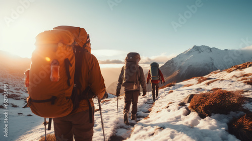 Rear view of three men in a row equipped with clothing and backpacks for a high mountain trek, walking on a snowy trail. Adventure sports concept