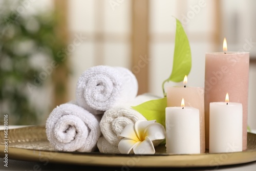 Spa composition. Burning candles, plumeria flower, green leaves and towels on table indoors