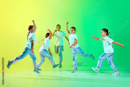 Cute children wearing fashion trendy outfit with bright glittered makeup dancing synchronous in motion over gradient background in neon light.