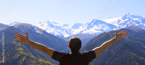 hands spread to the sides. male Hiker arms outstretched on mountain top. Man stands in snowy mountain covered pine forest. Man on peak of Caucasian Mountain. back rear view of young adult brunette guy