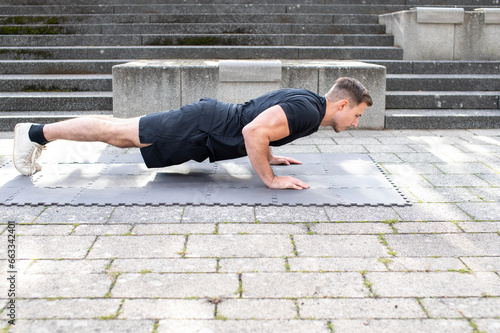 Sportive young man doing push-ups on concrete background outdoors.