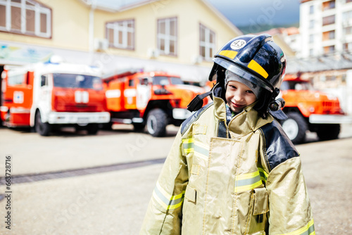 Child, cute boy, dressed in fire fighers cloths in a fire station with fire truck, childs dreamed profession