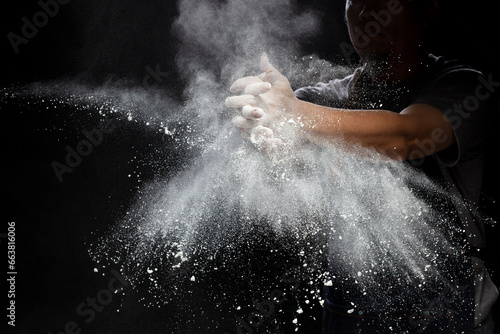 Chef prepare white flour dust for cooking bakery food. Elderly man Chef clap hand, white flour dust explode fly in air. Flour stop motion in air with freeze high speed shutter, black background