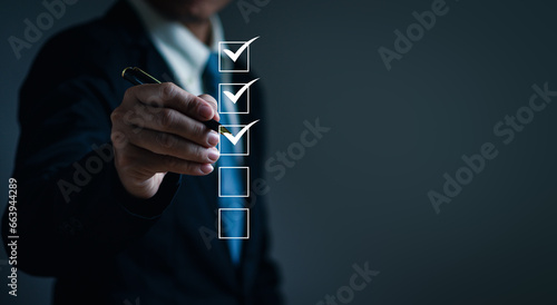 Businessman uses a pen to tick off checkboxes on a business performance checklist. Concept of filling out digital form checklists, doing assessments, questionnaires, clipboard task management