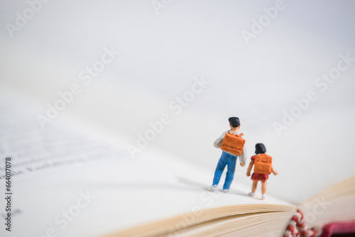 Schoolchildren with schoolbags walk on an open book, miniature figures scene