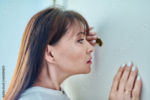 Serious middle-aged woman looking through peephole on front door
