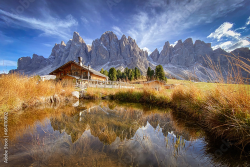 Scenic view of Geisler Alm Rifugio delle Odle in front of dolomites mountains and reflection in the water of a pond, South Tyrol, Italy