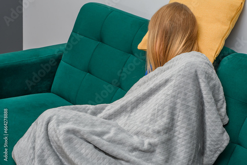 Zmęczona kobieta zasnęła na siedząco na sofie, przykryta kocem