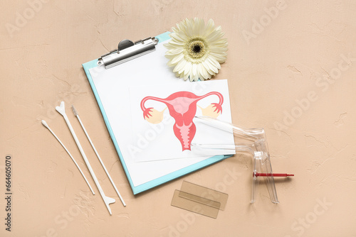 Gynecological speculum, drawing of female uterus, clipboard and pap smear test tools on beige background