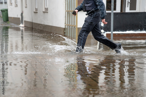Policeman running through the water of a flooded street during high water of the river Trave in the old town of Lubeck at the Baltic sea in Germany, copy space
