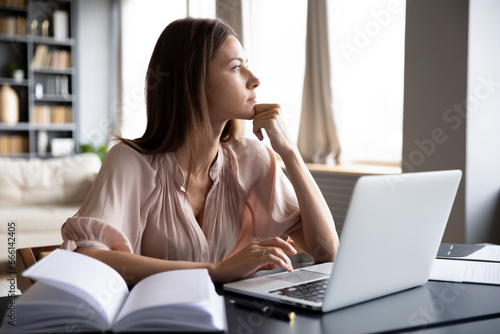 Pensive woman sit at table thinking looking out the window, housewife solve household issues using laptop personal organizer. Business lady makes decision distracted from typing email lost in thoughts