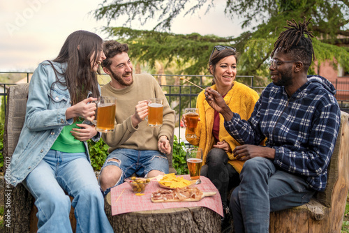 Outdoor Gathering with Friends - Friends laughing and drinking beers outdoors around a tree trunk table with snacks. Garden setting, relaxed atmosphere.