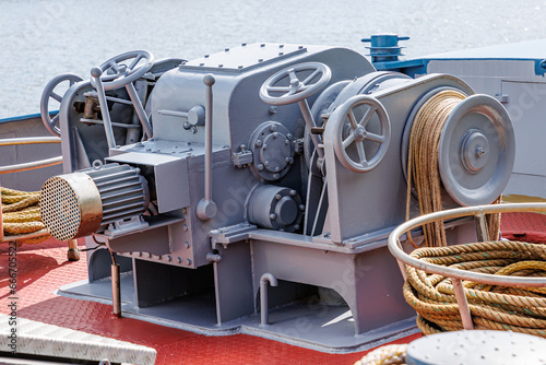 Closeup of a large ship control mooring station with levers, steering wheels, anchor windlass machine and heavy duty winches with tow rope on bow of a cargo ship, water in background blurred
