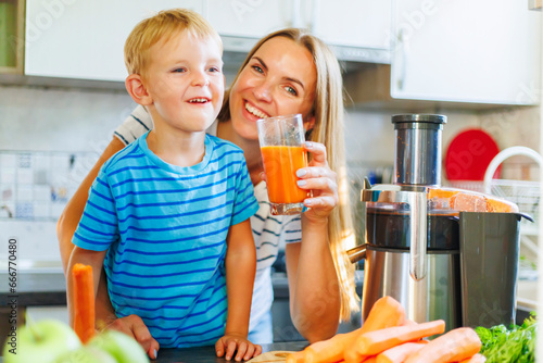 Mom and son drink fresh carrot juice squeezed using juicer in kitchen at home