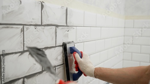 Working grouting of tiles, applying grout to the seam of tiles for home renovation in the kitchen. Applying grout to ceramic mosaic tiles. Working hands work with ceramic tiles.