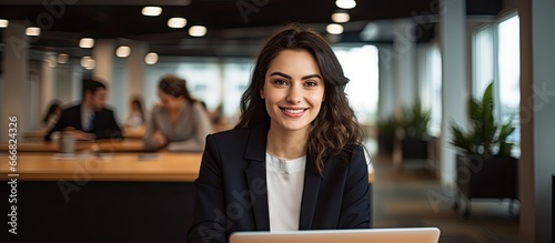 Attractive Hispanic woman in office smiling and looking at camera while using laptop