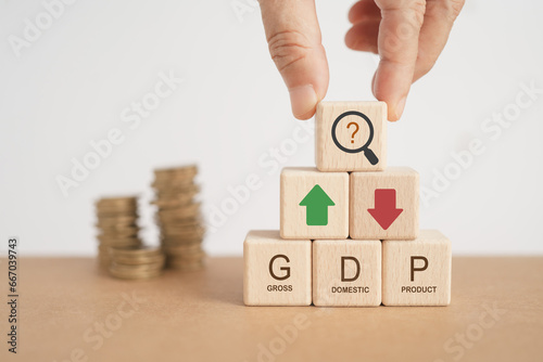 For global economy GDP text, gross domestic product , on stack of wooden cube block with up and down arrow and blurred coins