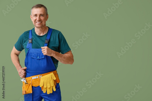 Portrait of male mechanic with tool belt on green background