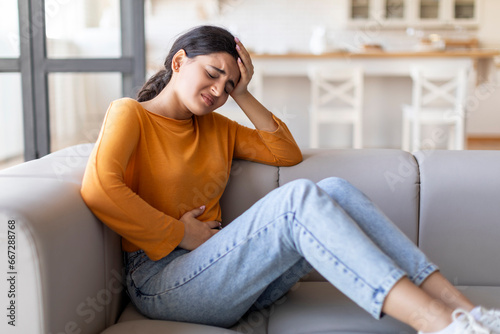 Sad young indian woman suffering from PMS and menstruation pain at home