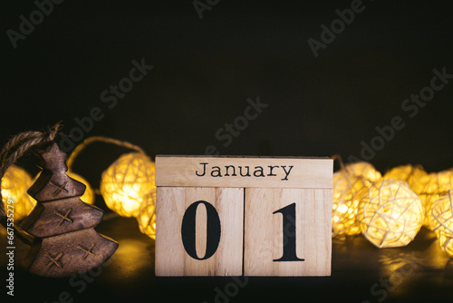 Brown wooden calendar on the black table with garland. Black background. Items to tell date, reminder, planner or meeting. Vintage idea shows 01 January, the beginning of the year. New Year day
