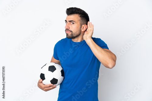 Handsome young football player man over isolated wall listening to something by putting hand on the ear
