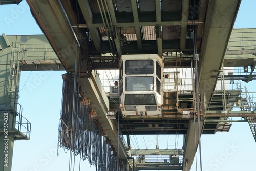 White cabin of green gantry crane operated by stevedores in Houston container terminal. There is upper part of construction of machinery and various cables.