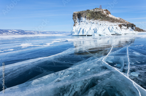 Baikal Lake on sunny frosty day in February. View from smooth blue ice with cracks to icy cliff of Horin-Irgi - natural landmark of Olkhon Island. Scenic winter landckape. Ice travel and outdoors