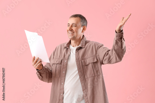 Mature actor with film script on pink background