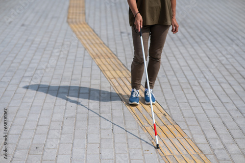 Close-up of the legs of an elderly blind woman with a cane at a tactile tile.