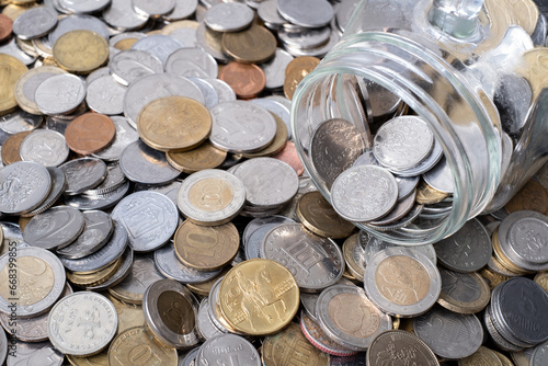 Various coins are falling out of a glass jar, concept of saving money.