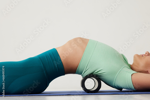girl massages her back on a roller and does yoga on a white background, massage roller for fitness and yoga, Home training