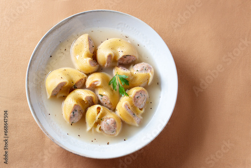 Traditional Catalan Christmas dish Escudella in white plate on table, stuffed pasta in meat broth, top view